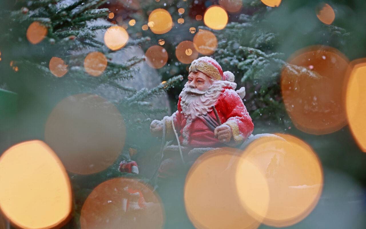 Blick durch eine Lichterkette auf eine schneebedeckte Weihnachtsmannfigur