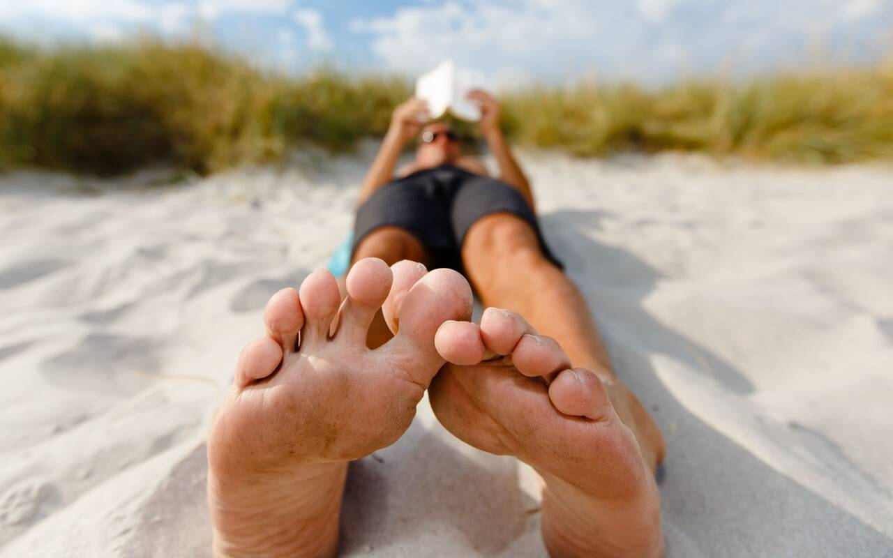 Ein Mann liegt am Ostseestrand und liest ein Buch.
