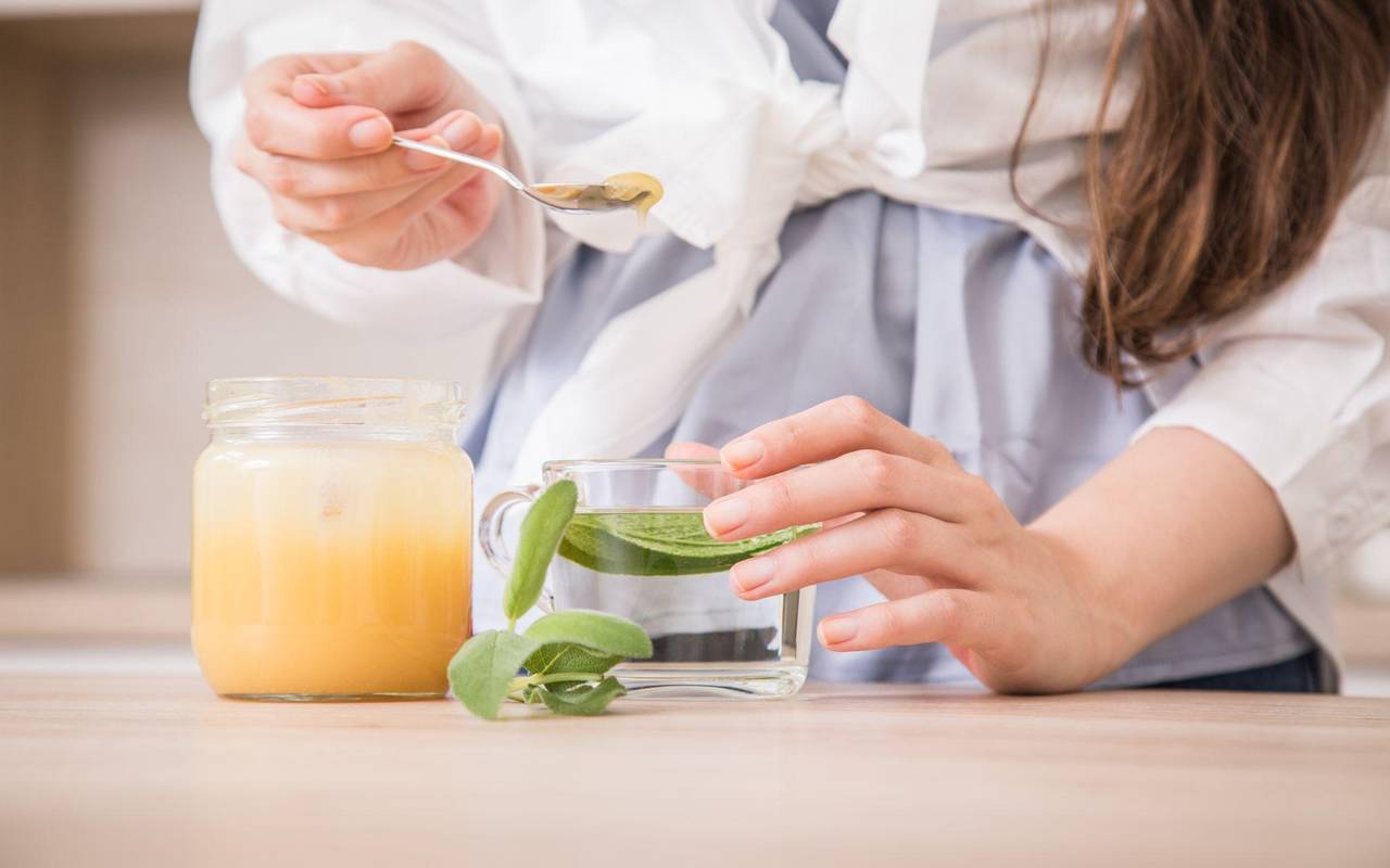 Eine Frau bereitet frischen Salbeitee mit Honig zu