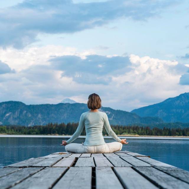 Eine Frau sitzt auf einem Steg und meditiert