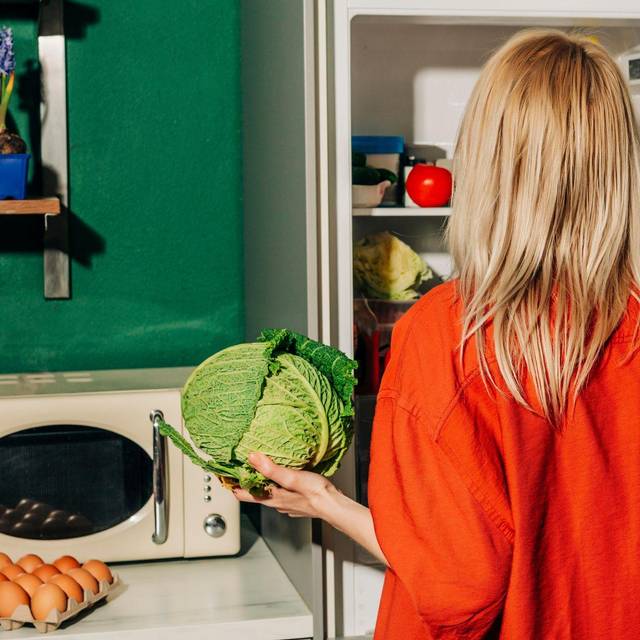 Eine Frau hält einen Kohl vor einem offenen Kühlschrank