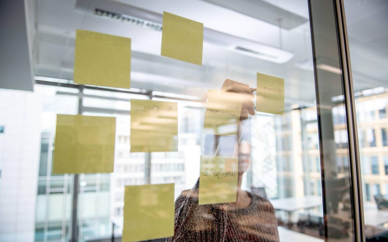 Eine Person klebt einen gelben Notizzettel an eine Glaswand