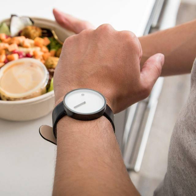 Ein Mann mit einem Teller in der Hand sieht auf seine Uhr