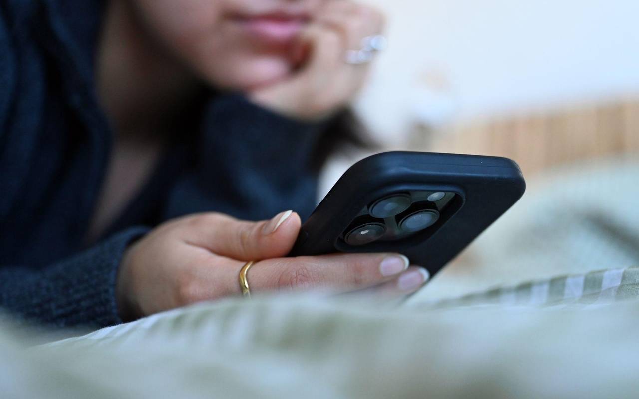 Frau liegt auf einem Bett und schaut auf ihr Smartphone