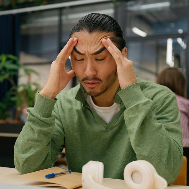 Ein Mann fasst sich an die Schläfen in einem Großraumbüro