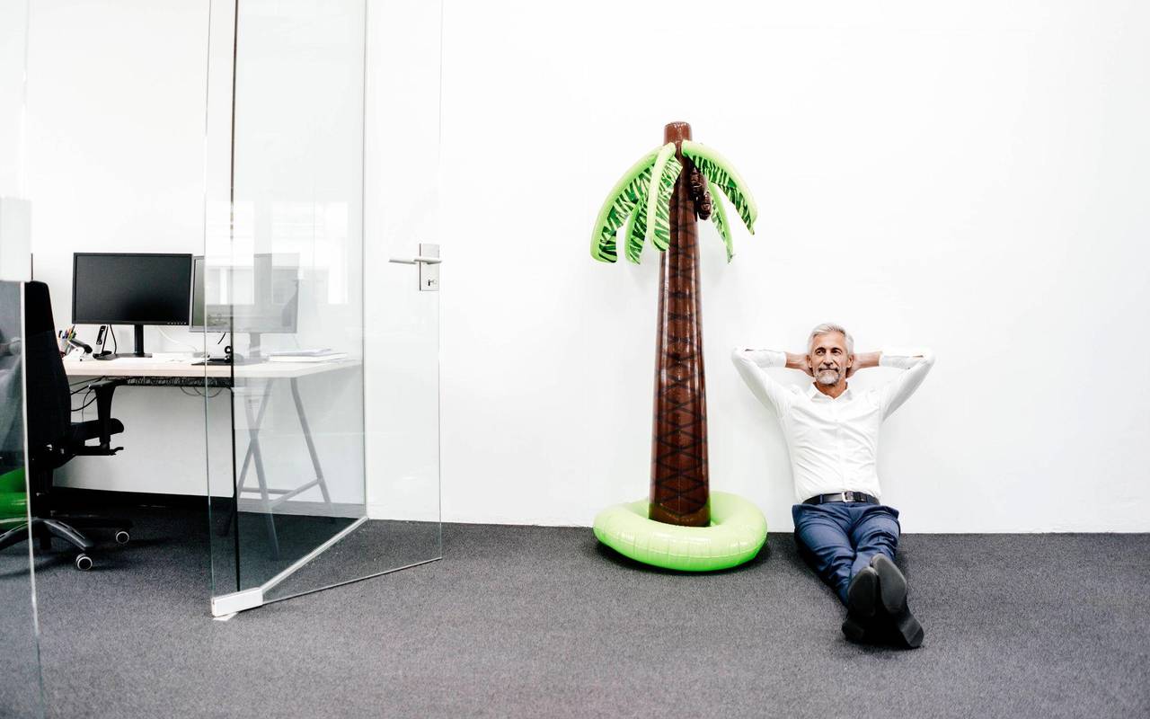 Mann sitzt im Büro neben einer aufblasbaren Palme