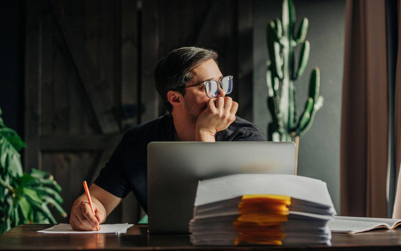 Ein Mann arbeitet am Laptop und sieht aus dem Fenster