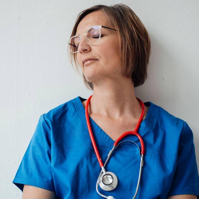 Eine Ärztin lehnt mit geschlossenen Augen an der Wand