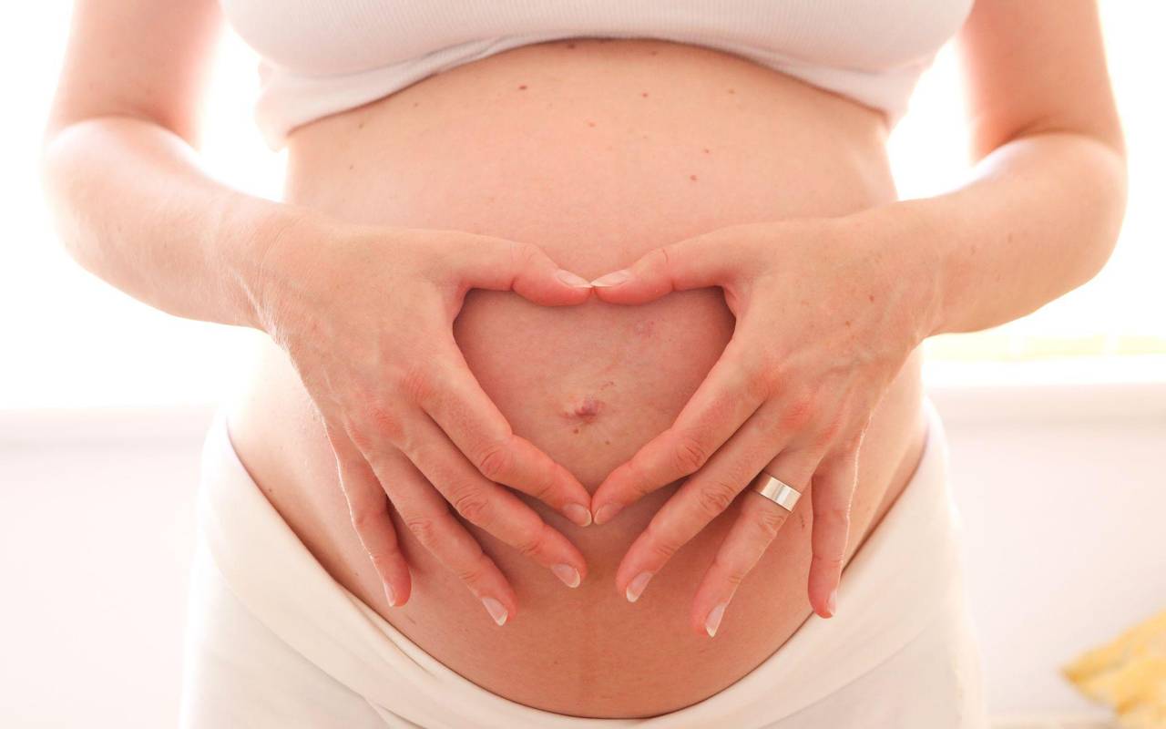 Eine schwangere Frau hält zum Herz geformten Hände vor den Bauch
