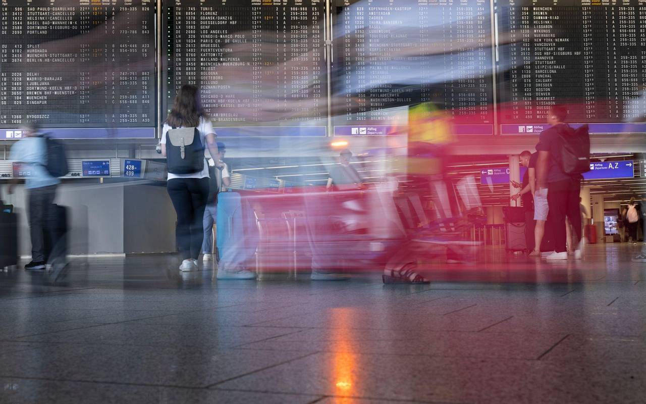 Passagiere gehen vor der Anzeigetafel im Flughafen entlang