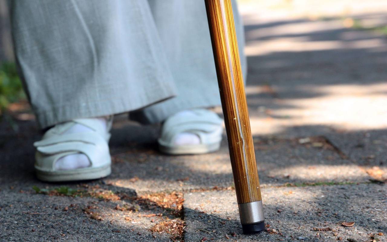 Eine Frau steht mit einem Stock auf einem Gehweg