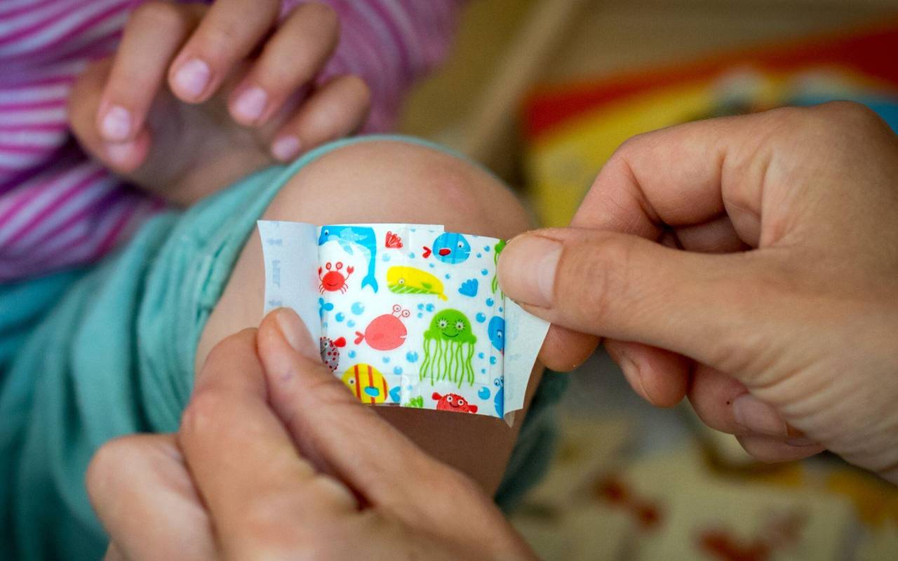 Eine Mutter klebt ihrer Tochter ein buntes Pflaster aufs Knie