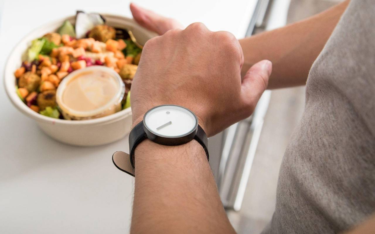 Mann mit einem Salat in der Hand schaut auf seine Armbanduhr