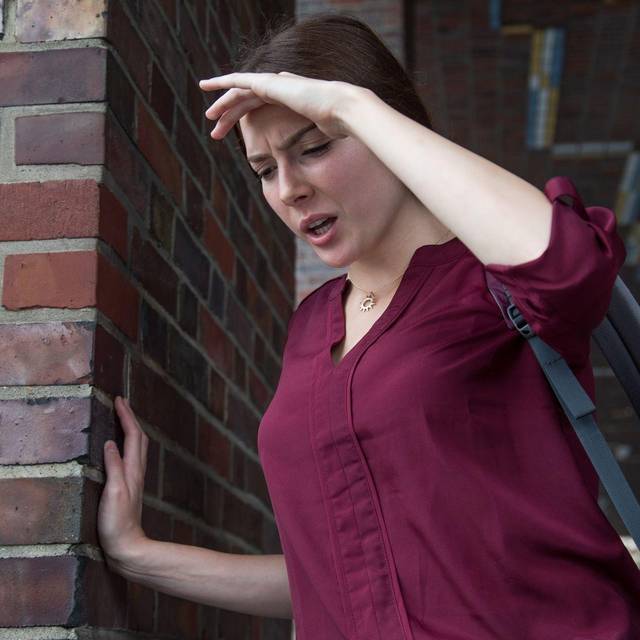 Frau stützt sich an einer Wand ab, weil ihr schwindelig ist