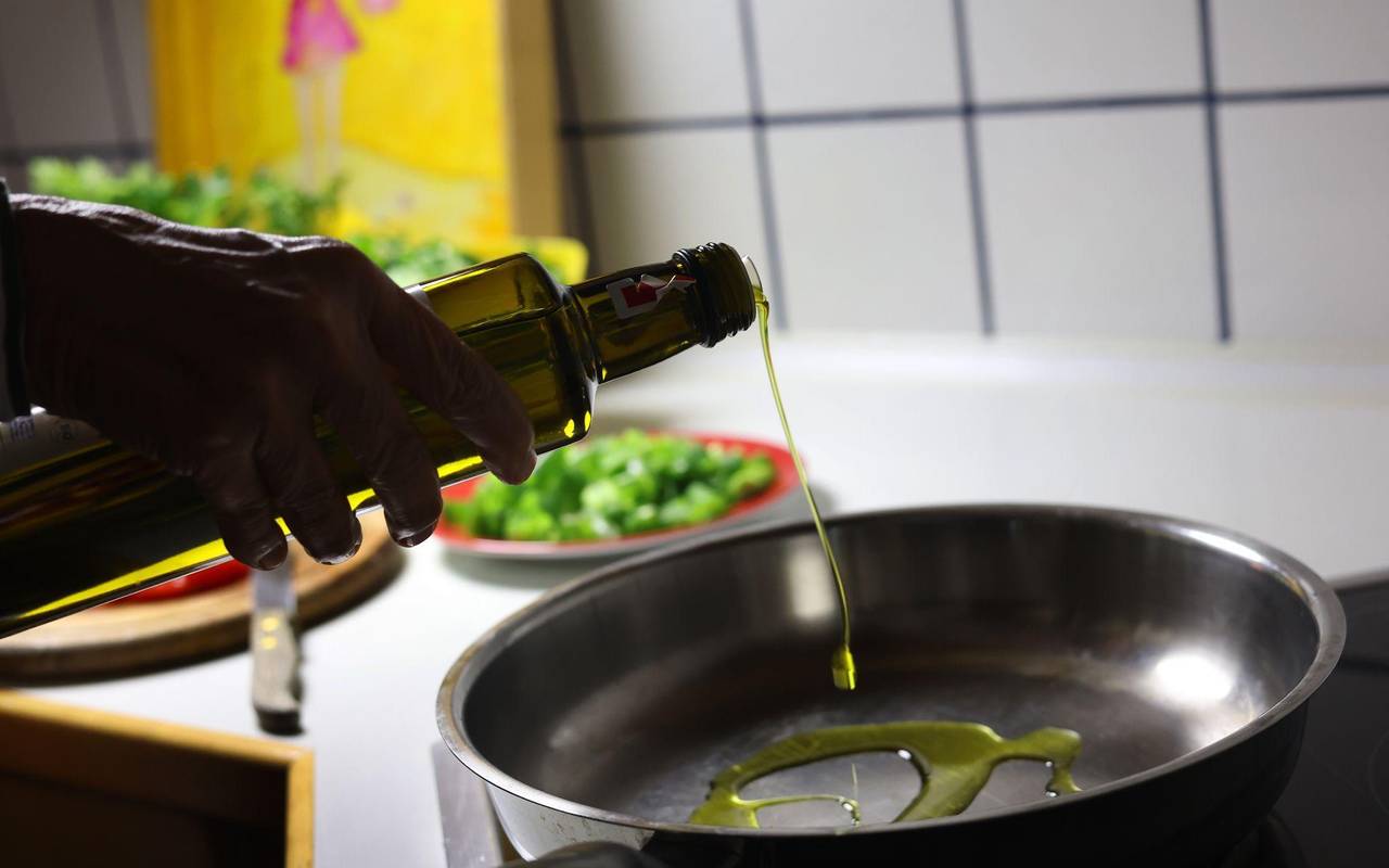 Frau gibt beim Kochen Olivenöl in eine Pfanne