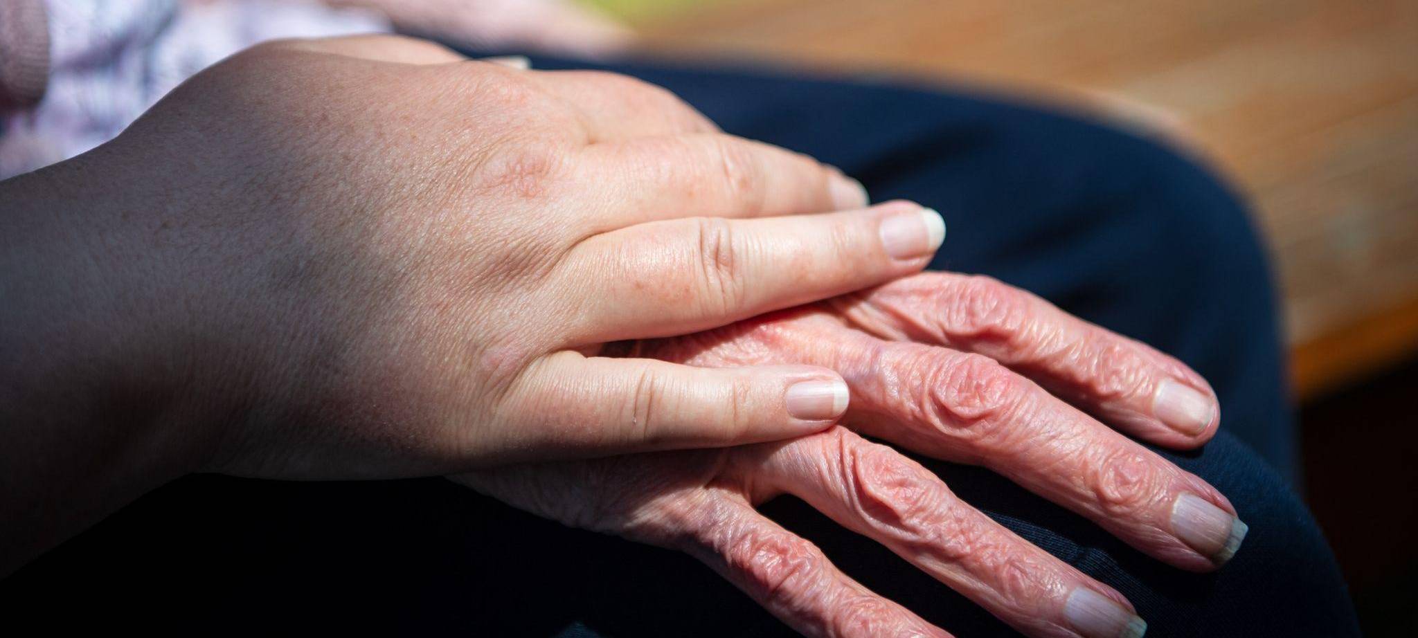 Hand einer Pflegefachkraft liegt auf Hand eienr Seniorin