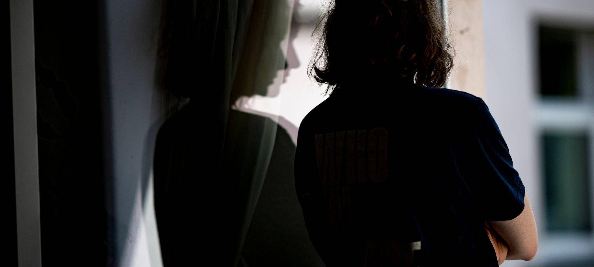 Frau steht mit verschränkten Armen in ihrer Wohnung am Fenster