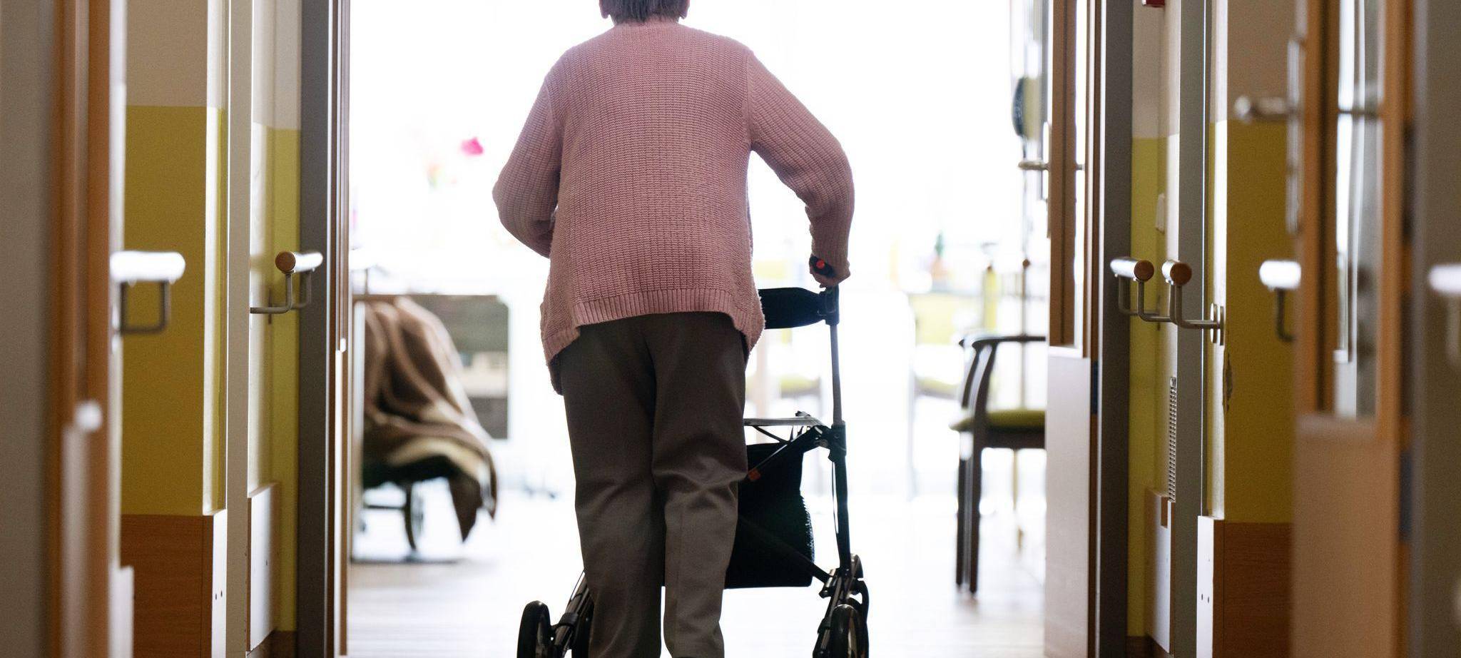 Eine Frau geht mit einem Rollator in einem Altenheim