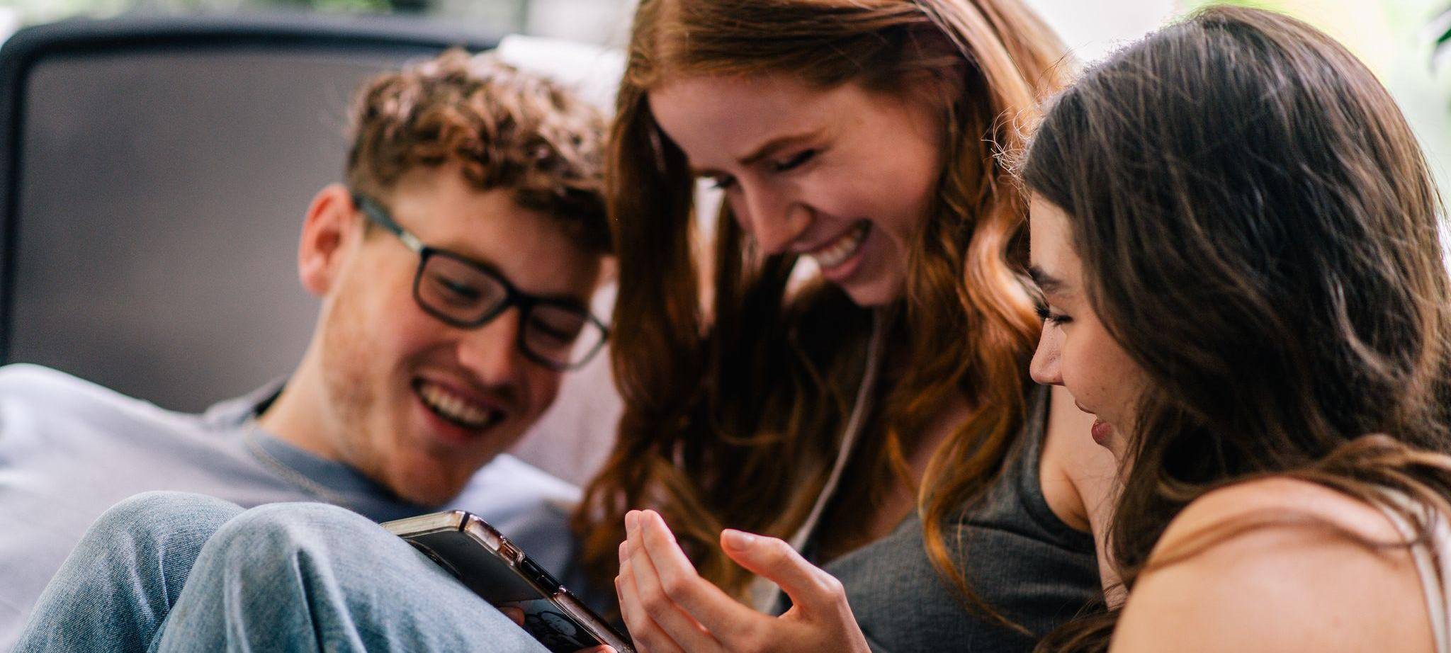 Freunde blicken lachend auf ein Smartphone